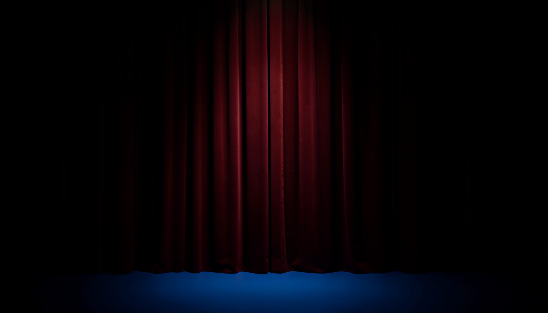 Warm stage spotlight on a deep burgundy curtain, rich amber glow fading into dark shadows, theatrical and inviting atmosphere
