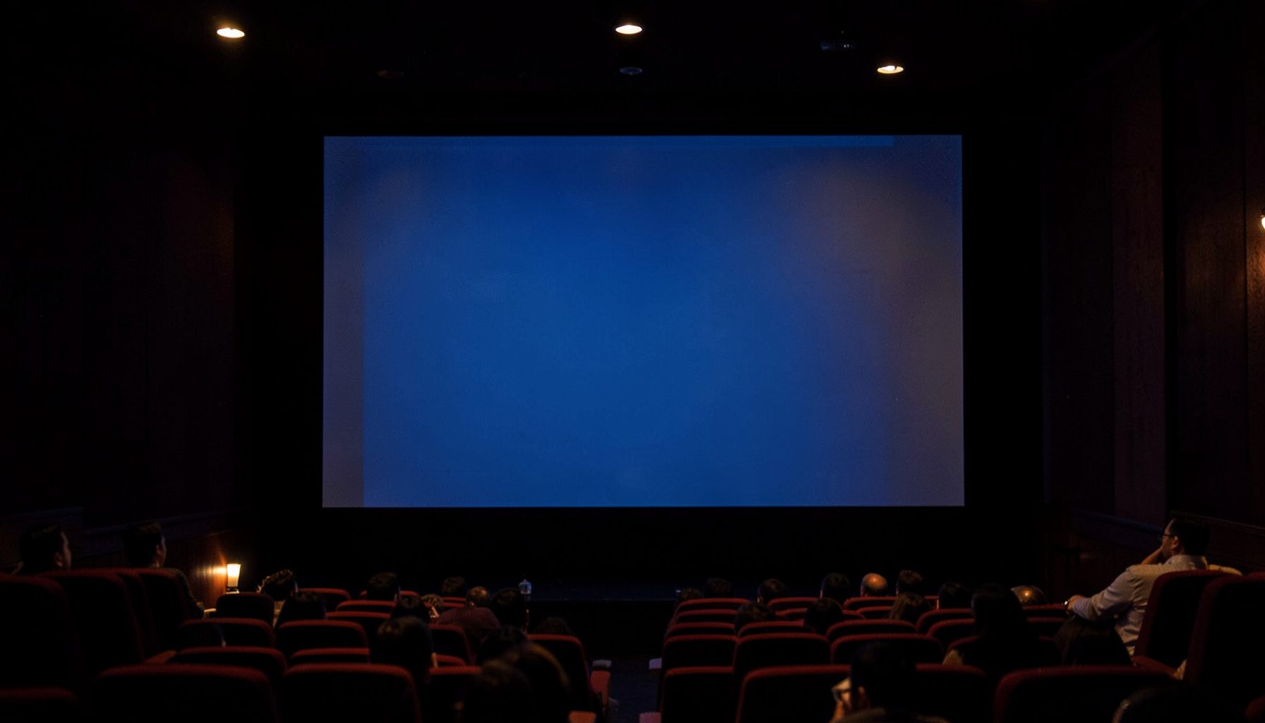 A softly lit cinema screen with warm amber and deep navy tones, evoking the feel of Indian film entertainment.