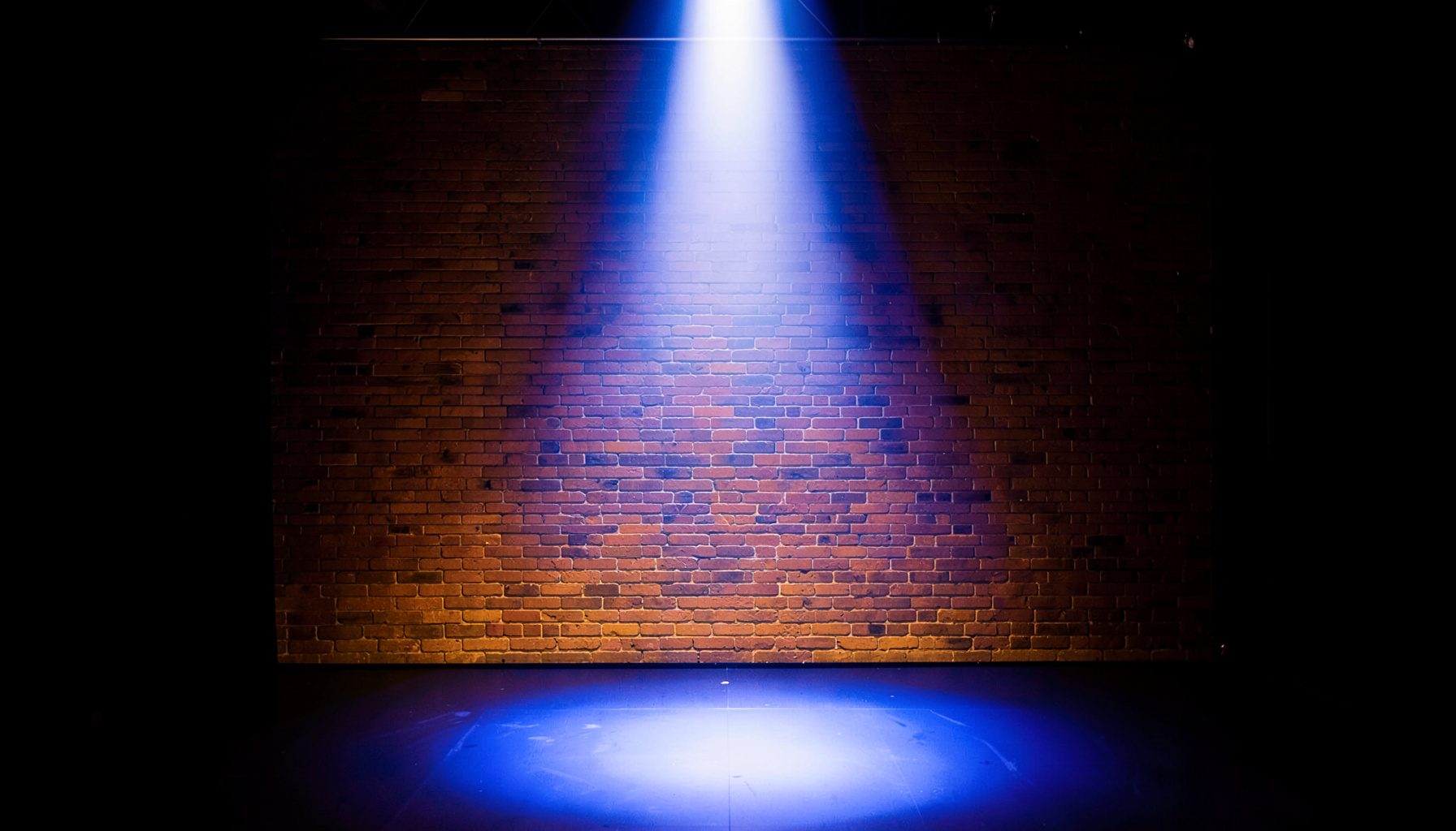 Comedy club stage with spotlight and brick wall backdrop, warm amber glow