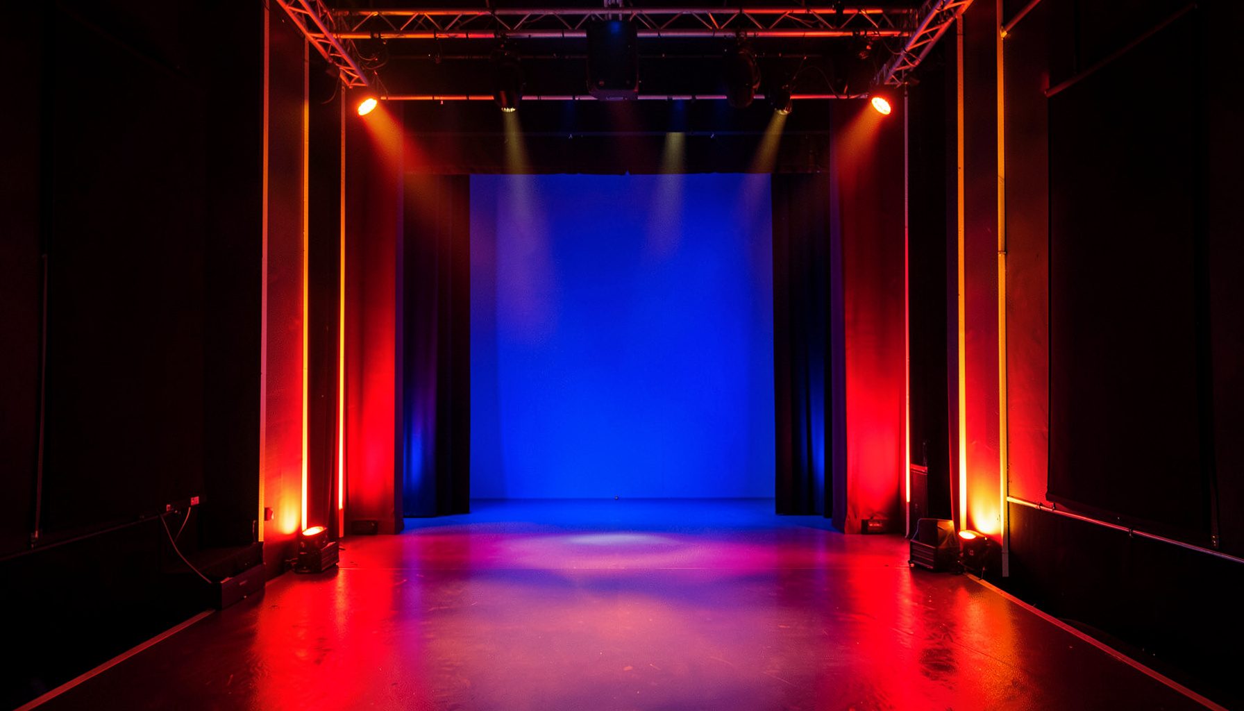 Bright studio set with colorful comedy stage lighting, warm red and gold tones